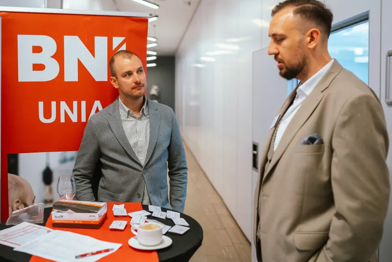 Rozmowa przy stoliku rejestracji obok rollupu BNI UNIA