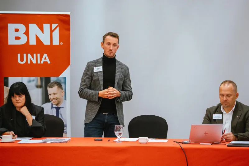 Wystąpienie przy stole prowadzących, obok rollup BNI UNIA